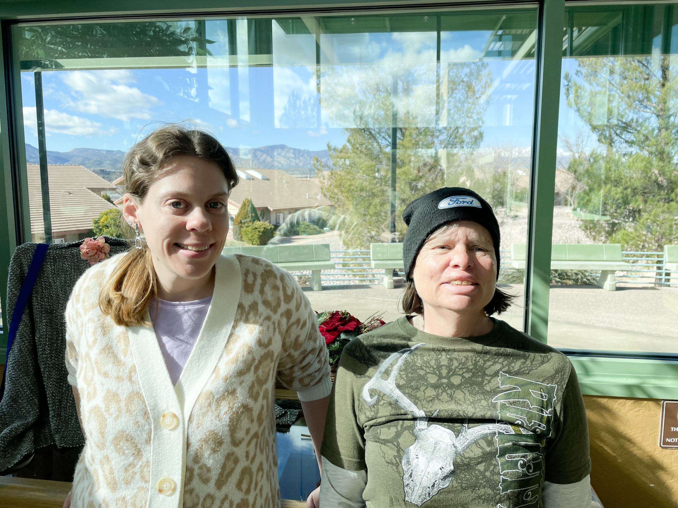 Resident Ranchers, Julie and Kelly, stand in front of a window at Rainbow Acres and pose for a picture. Rainbow Acres is a residential Christian community for adults with developmental disabilities. Some of the neurodiverse residents are diagnosed with autism, down syndrome, adhd, depression, anxiety, PTSD, and many other disorders.