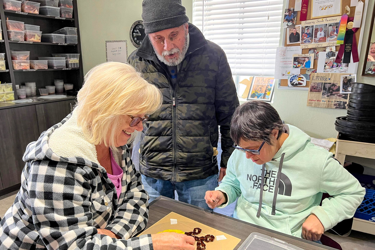 A Caregiver works with several resident Ranchers to create a design for a stepping stone with scrap colored glass. The scrap glass is donated from the Sun City West Stained Glass Crafters.